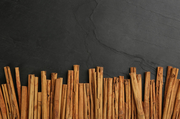 Aromatic cinnamon sticks on black table, flat lay. Space for text - Foto, afbeelding