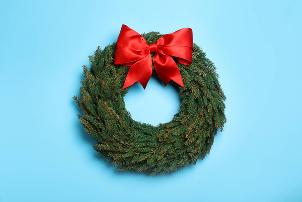 Christmas wreath made of fir branches with red bow on light blue background, top view - Fotografie, Obrázek