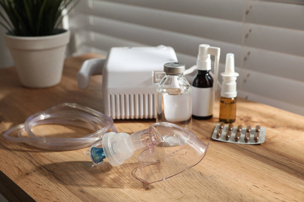 Modern nebulizer with face mask and medications on wooden table indoors. Inhalation equipment - Фото, изображение