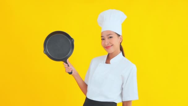 muotokuva kaunis nuori aasialainen kokki tilalla paistinpannu keltaisella pohjalla - Materiaali, video