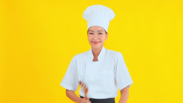 retrato de belo jovem chef asiático segurando espátula de madeira no fundo amarelo - Filmagem, Vídeo