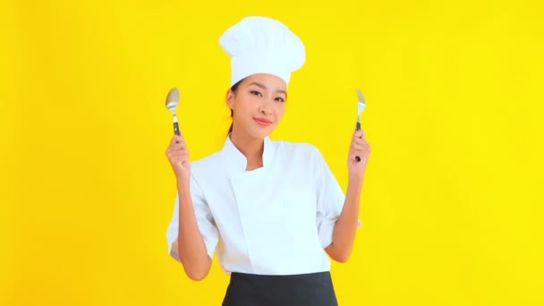 portret van mooie jonge Aziatische chef met vork en lepel op gele achtergrond - Video