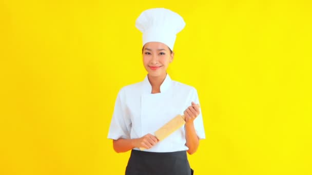 Sarı arka planda merdanesi olan genç ve güzel bir Asyalı aşçının portresi. - Video, Çekim