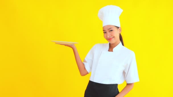 muotokuva kaunis nuori aasialainen kokki tilalla tyhjä levy keltaisella pohjalla - Materiaali, video
