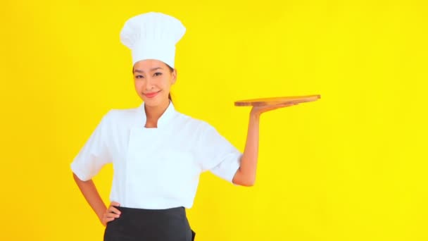 portret van mooie jonge Aziatische chef-kok houden snijplank op gele achtergrond - Video