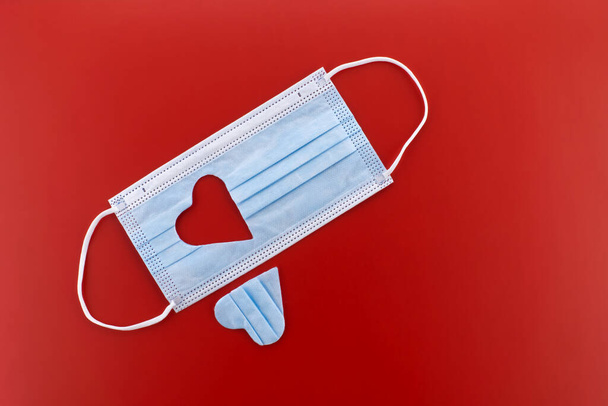 Μάσκα προσώπου με κομμένο σχήμα καρδιάς σε κόκκινο φόντο με ελεύθερο χώρο αντιγραφής - Φωτογραφία, εικόνα