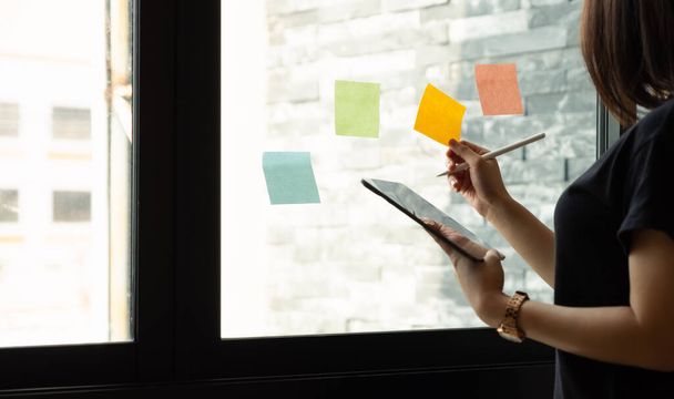 donna d'affari che utilizza tablet durante post annota l'idea di discutere e pianificare in parete di vetro in sala riunioni, concetto di business. - Foto, immagini