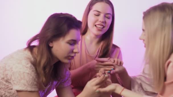 Τέσσερις χαρούμενες όμορφες γυναίκες με πιτζάμες κάθονται στο κρεβάτι και επιδεικνύουν τα νύχια τους η μία στην άλλη στο μπάτσελορ πάρτι. - Πλάνα, βίντεο