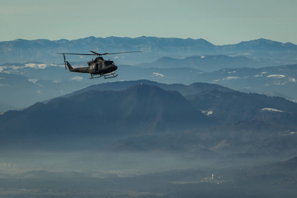 Leger redding helikopter zweven met zijdeur open aan de hemel in de voorkant van een prachtige schilderachtige achtergrond met heuvels en bergkammen. - Foto, afbeelding