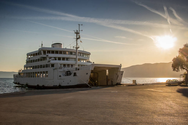 Een Kroatische veerboot afgemeerd op het eiland Cres in de late namiddag wachten op voertuigen, met de zon langzaam onder achter de bergen op de achtergrond. - Foto, afbeelding