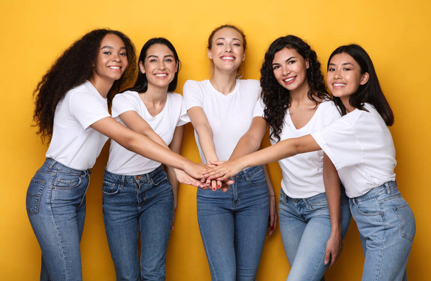 Πέντε χαρούμενες διαφορετικές γυναίκες κρατώντας τα χέρια στέκεται σε κίτρινο φόντο - Φωτογραφία, εικόνα
