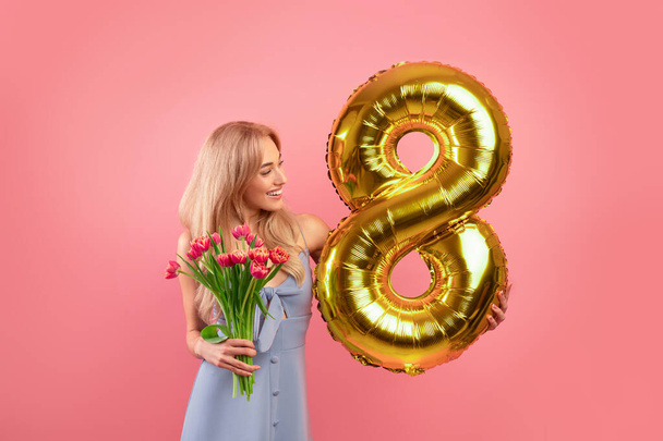 Seksikäs nuori nainen kukkia ja kultainen ilmapallo muotoinen numero kahdeksan vaaleanpunainen studio tausta - Valokuva, kuva