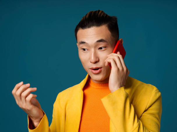Interested Korean man talking on the phone on a blue background and gesturing with his hands - Foto, Imagen