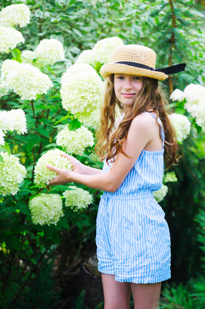 happy kid girl walking in blooming summer garden, posing near white hydrangea paniculata bush - Zdjęcie, obraz