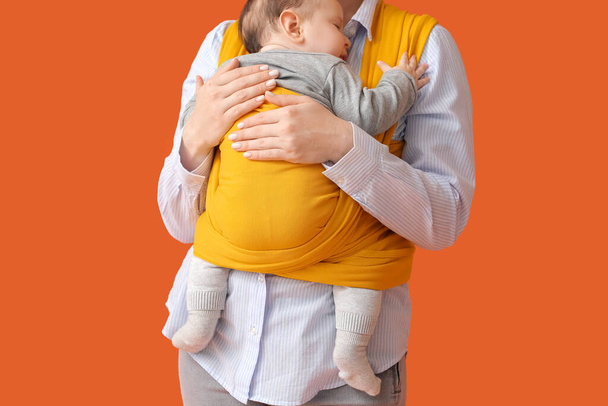 Νεαρή μητέρα με μικρό μωρό σε σφεντόνα στο φόντο χρώμα - Φωτογραφία, εικόνα