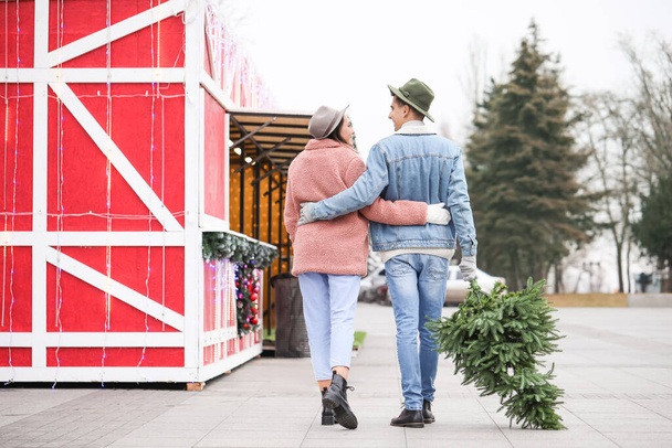 Happy young couple with fir tree on Christmas fair outdoors - Photo, Image