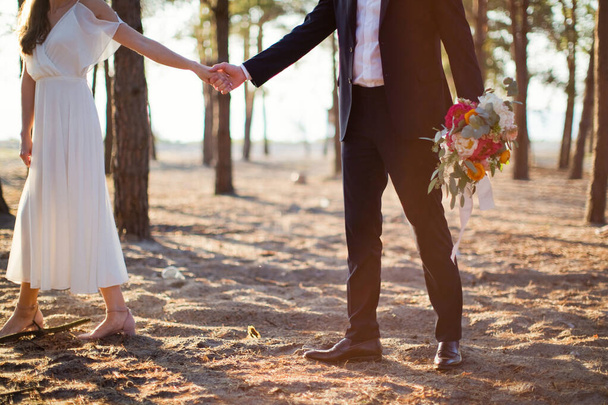 花嫁と新郎は手を取り合い、日没の光で海の近くを歩く - 写真・画像