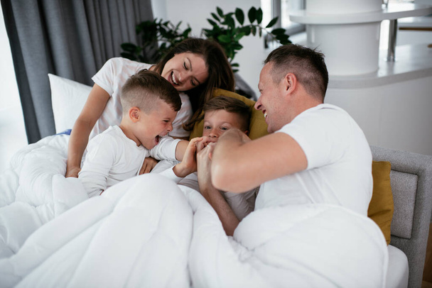 若い家族がベッドで楽しんでいる。ベッドでリラックスしている息子と幸せな両親 - 写真・画像
