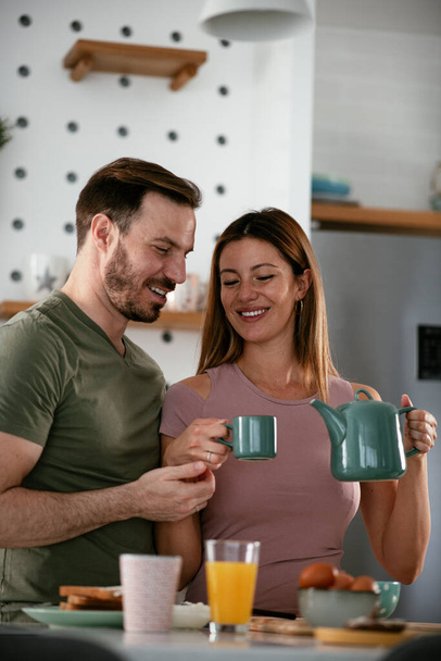 Amar pareja bebiendo café mientras se prepara el desayuno. - Foto, Imagen