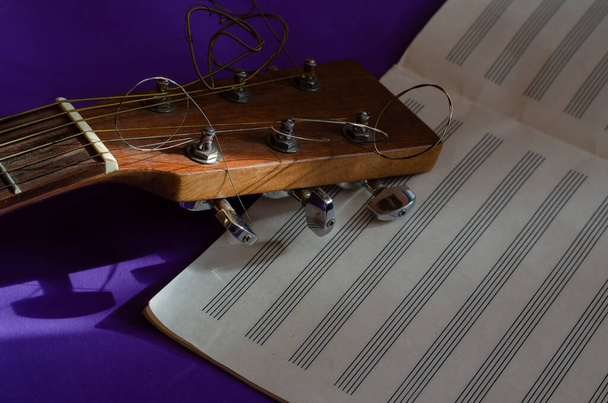 Primo piano di una testa di tastiera di chitarra acustica e notebook di musica aperta su uno sfondo blu. Luce del sole su uno strumento musicale. Creatività musicale. - Foto, immagini