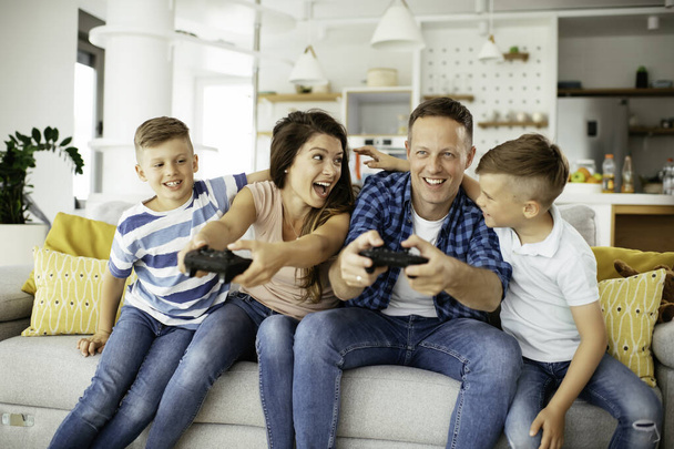  Счастливая любящая пара играет в видеоигры с детьми дома. - Фото, изображение