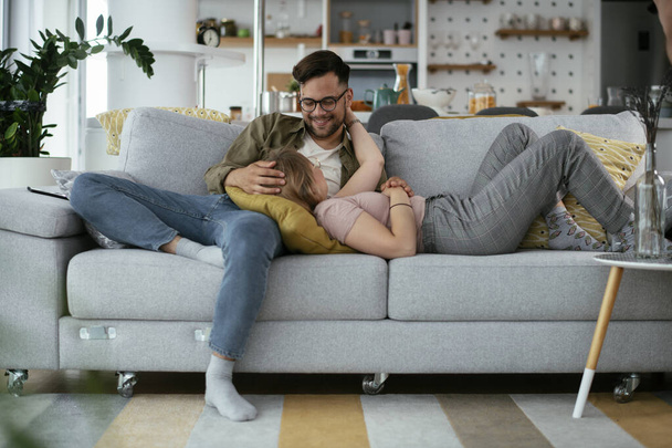 Mladý milující pár si užívá na gauči. Šťastný pár relaxaci v obývacím pokoji.. - Fotografie, Obrázek