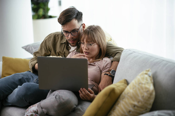 Młoda para ogląda film na laptopie. Kochająca para ciesząca się w domu. - Zdjęcie, obraz