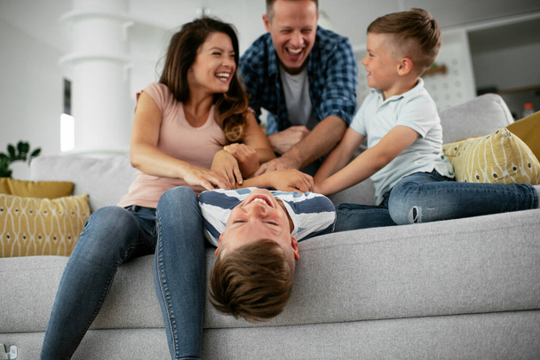 Νεαρή οικογένεια απολαμβάνει το σπίτι της. Ευτυχισμένοι γονείς με γιους που διασκεδάζουν. - Φωτογραφία, εικόνα