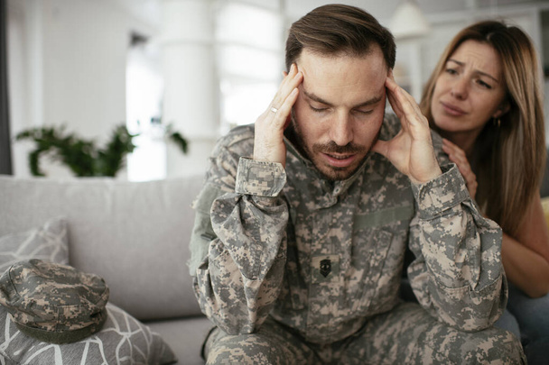 Καταθλιπτικός στρατιώτης που κάθεται στον καναπέ με τη γυναίκα του. Νεαρός πεζοναύτης με μετατραυματικό στρες. - Φωτογραφία, εικόνα