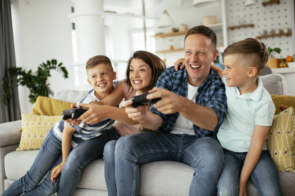 Πατέρας και μητέρα διασκεδάζουν παίζοντας βιντεοπαιχνίδια με παιδιά στο σπίτι. - Φωτογραφία, εικόνα