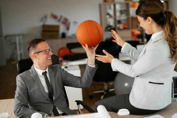 Businessman and businesswoman wit basketball in office. Beautiful woman and handsome man having fun at work. - Фото, зображення