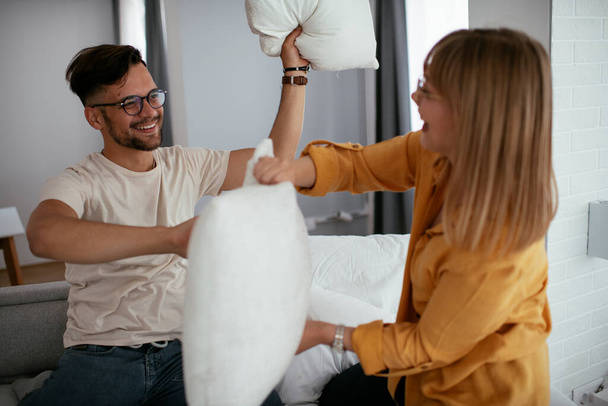 Young couple fighting pillows on the bed. Happy couple having fun at home - Valokuva, kuva