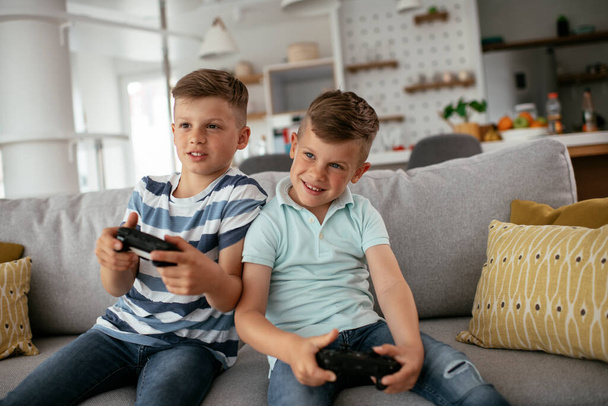 Young brothers having fun while playing video games in living room - Photo, Image