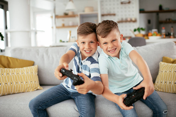 Onnelliset veljet pelaamassa videopelejä. Nuoret veljet hauskaa pelatessaan videopelejä olohuoneessa - Valokuva, kuva