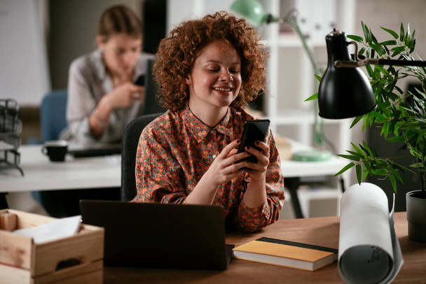 young woman with curly hair using phone in the office - Photo, Image