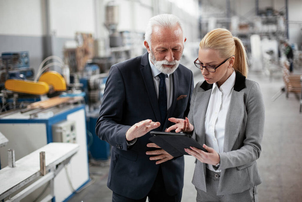 Businesswoman showing information about factory on tablet for businessman. Man and woman discussing work. - Fotoğraf, Görsel