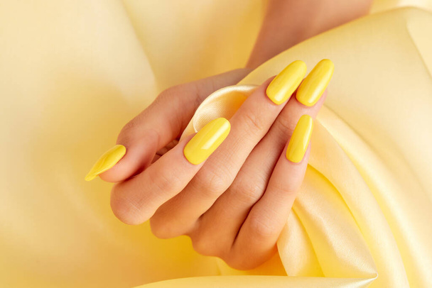 A closeup shot of a female's hand with yellow nail polish on a yellow silk fabric - Photo, Image