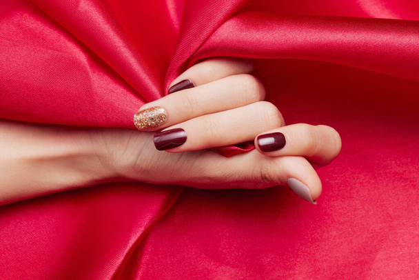 A closeup shot of a female's hand with beautiful nail polish caressing a red silk fabric - Foto, Imagem