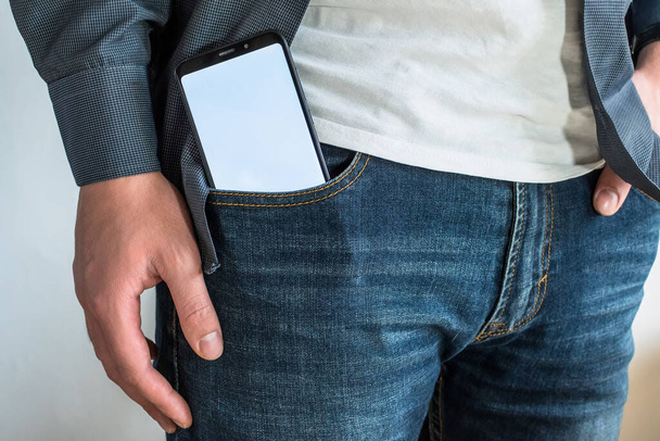 Eine Nahaufnahme eines Smartphones mit weißem Bildschirm im Rücken eines erwachsenen Mannes - Foto, Bild