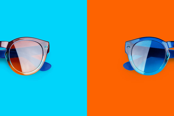 Sunglasses vibrant blue and orange red background close up top view, fashion sunshades on colorful backdrop, trendy modern eyeglasses, summer beach holidays concept, ultraviolet protection, copy space - Photo, Image