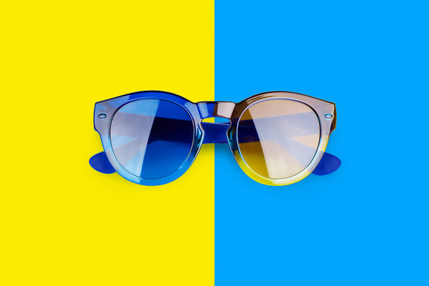 Óculos de sol em fundo azul e amarelo vibrante close-up vista superior, sunshades de moda em pano de fundo colorido, óculos modernos da moda, conceito de férias na praia de verão, proteção ultravioleta, espaço de cópia - Foto, Imagem