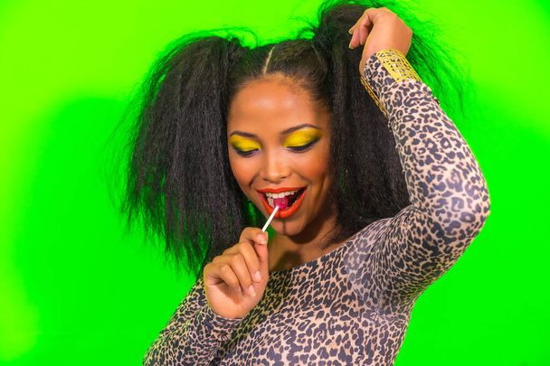 A closeup of a young pretty Hispanic girl with bright makeup and two tails hairstyle posing at the camera with a lollipop - Foto, Imagen
