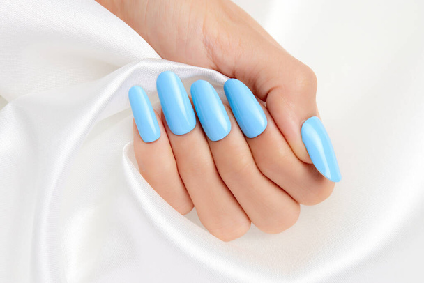 A closeup shot of a female's hand with blue nail polish on a white silk fabric - Foto, Imagem