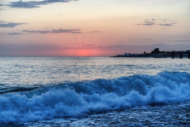 Puesta de sol sobre el mar en colores rosados y olas en la orilla. Vacaciones en el mar  - Foto, Imagen