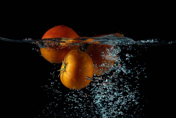 A closeup view of a red tomato dropped into the water creating a splash on a black background - Foto, immagini