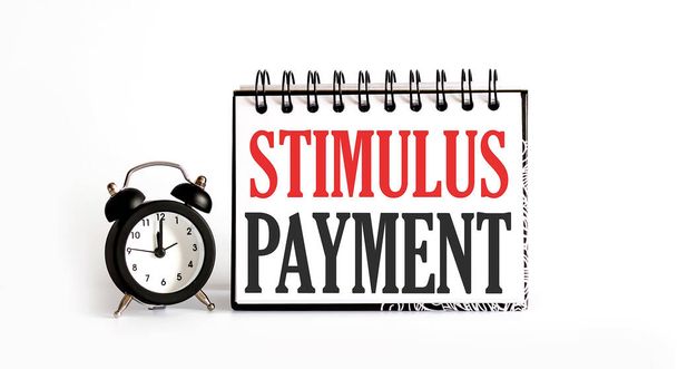 Bloc-notes de paiement Stimulus écrit sur fond blanc avec réveil - Photo, image