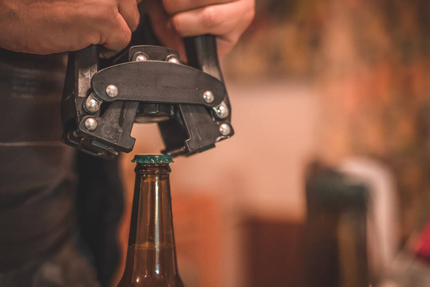 Detail of a tool for closing or bottling beer bottles. Man closing a beer bottle with a cap. Tool for closing craft beer bottle. - Фото, изображение