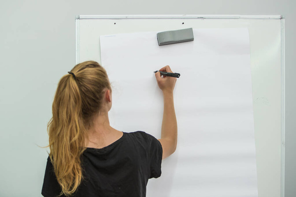 Junge Frau sieht Schreiben mit Stift auf Whiteboard oder Papier. Fokus auf den Stift, Blick von hinten - Foto, Bild