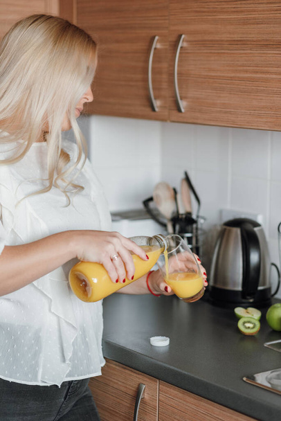 A vertical shot of a blonde woman pouring a glass of orange juic - Foto, Imagem