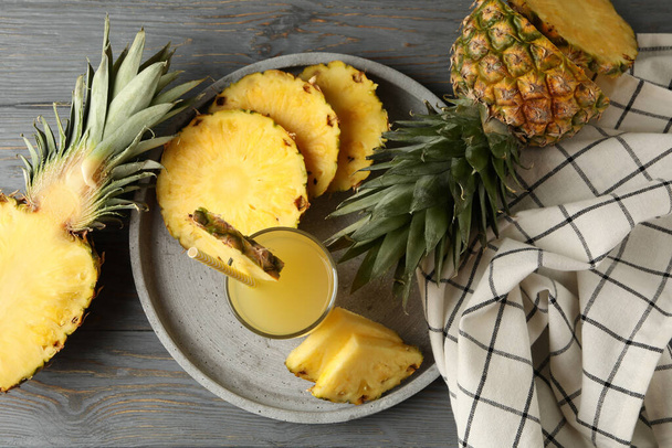 Tálca ananászszeletekkel és egy pohár gyümölcslével fából készült háttéren, felülnézet - Fotó, kép